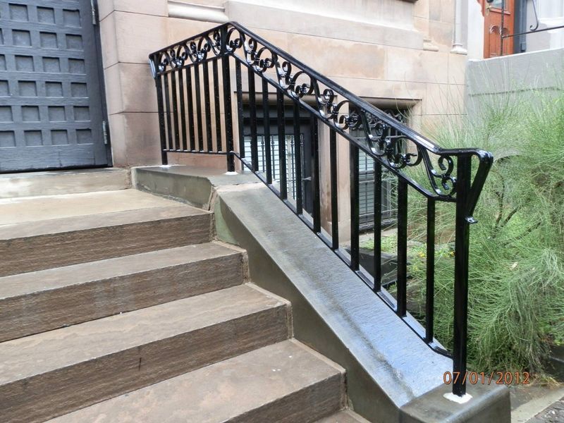 Black decorative metal handrail with scrollwork atop a concrete stoop next to a building entrance.