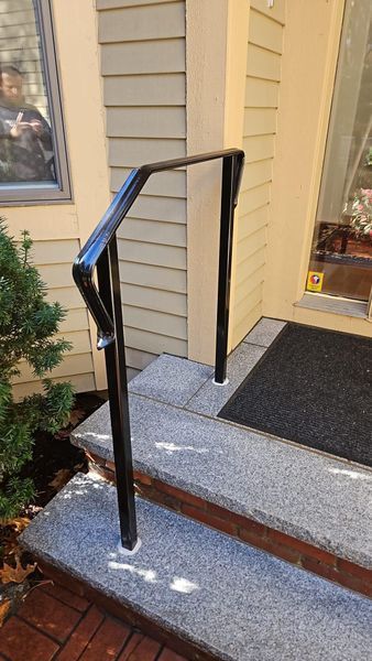 Black metal handrail installed on granite porch steps next to a house exterior.
