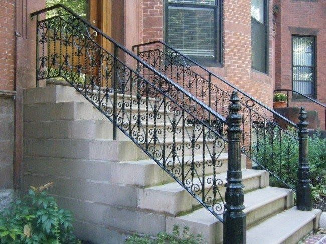 Stone steps with ornate black iron railings lead to the entrance of a brick building.