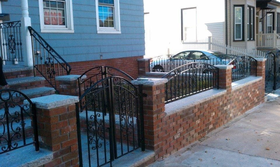 A residential front yard features a low brick wall topped with ornate black metal fencing and a matching gate.