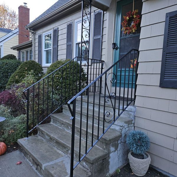 Exterior of a house with stone steps, black wrought iron railings, tan siding, and a festive fall wreath on the door.