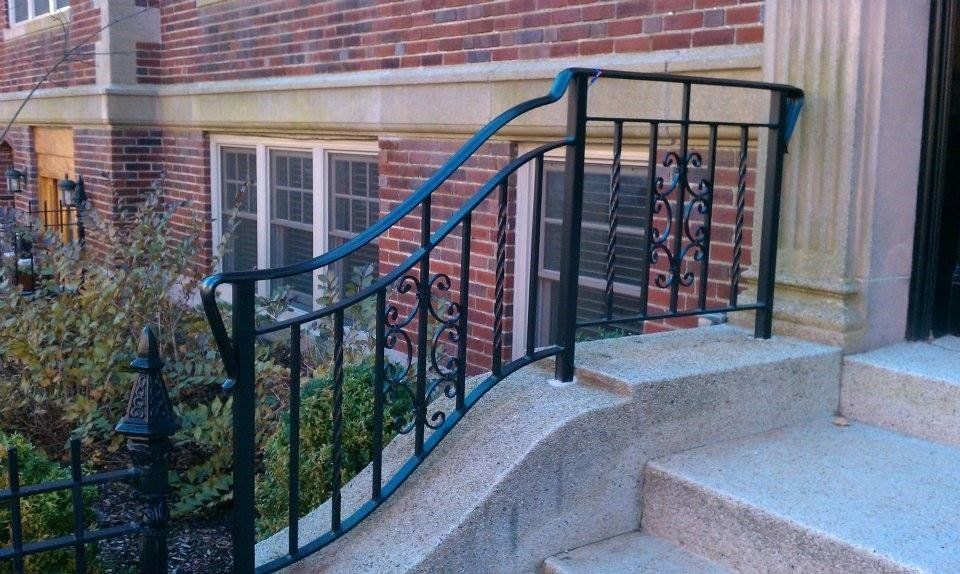 Black ornamental metal railing on concrete steps leading to a brick building entrance.