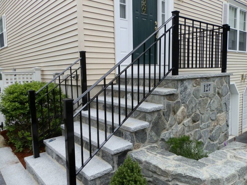 Concrete steps with black metal railings leading to a house entrance with stone foundation and light yellow siding.