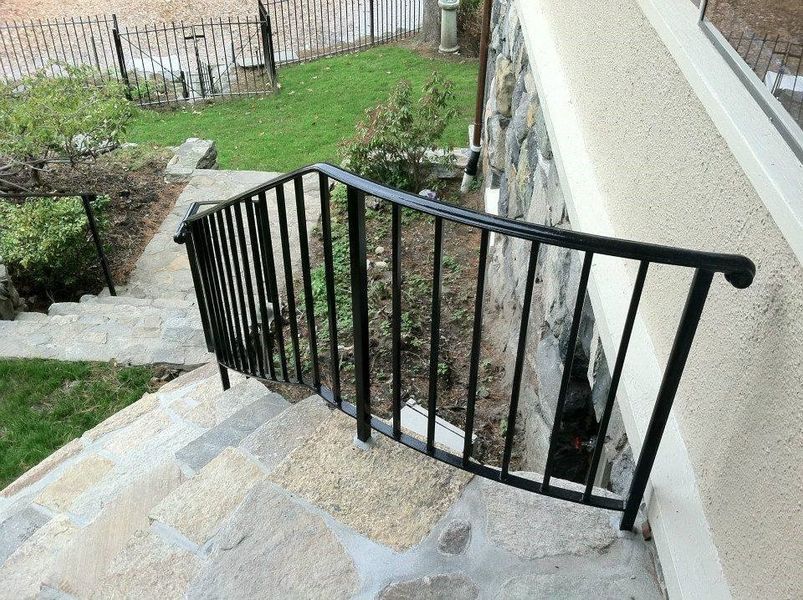 Black metal railing along outdoor stone stairs next to a stone-clad house wall.
