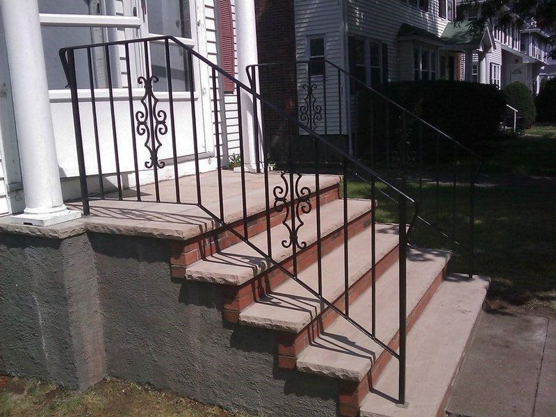 Concrete steps leading to a house entrance, featuring black decorative metal railings on both sides.