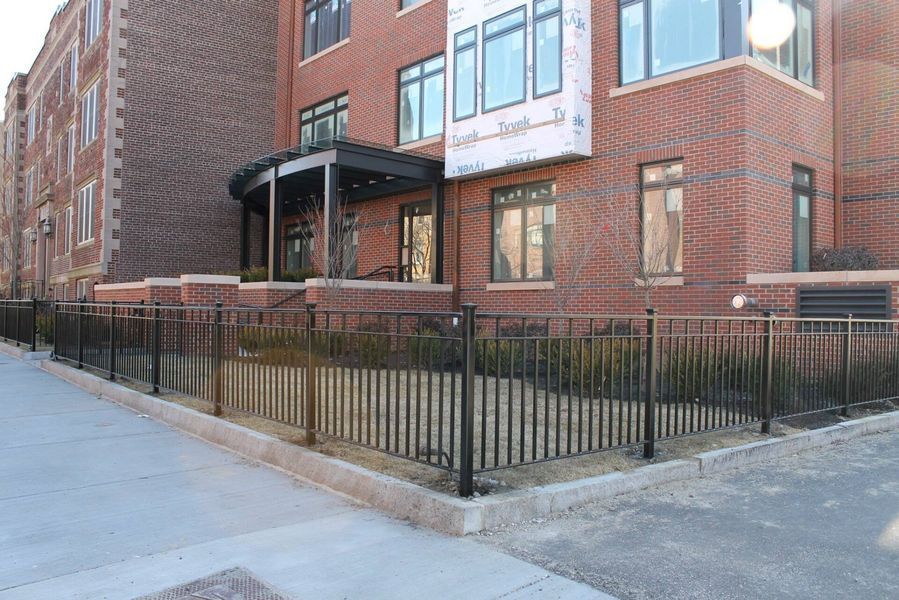 A red brick residential building with a black metal fence enclosing a small front lawn area.