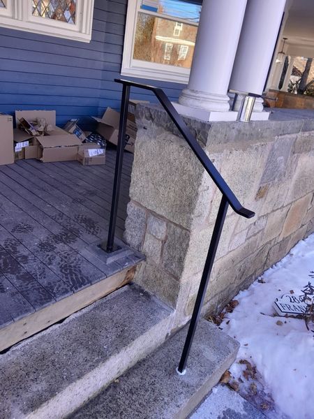 A black metal handrail installed alongside stone steps on a porch, leading up to a house entrance.