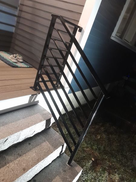 Black metal handrail installed on a small set of outdoor stone steps leading to a wooden deck.
