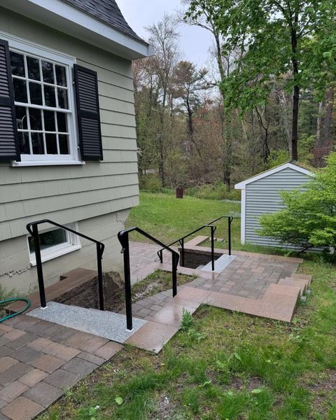 A beige house exterior features black handrails lining stone steps leading down to a basement entrance.