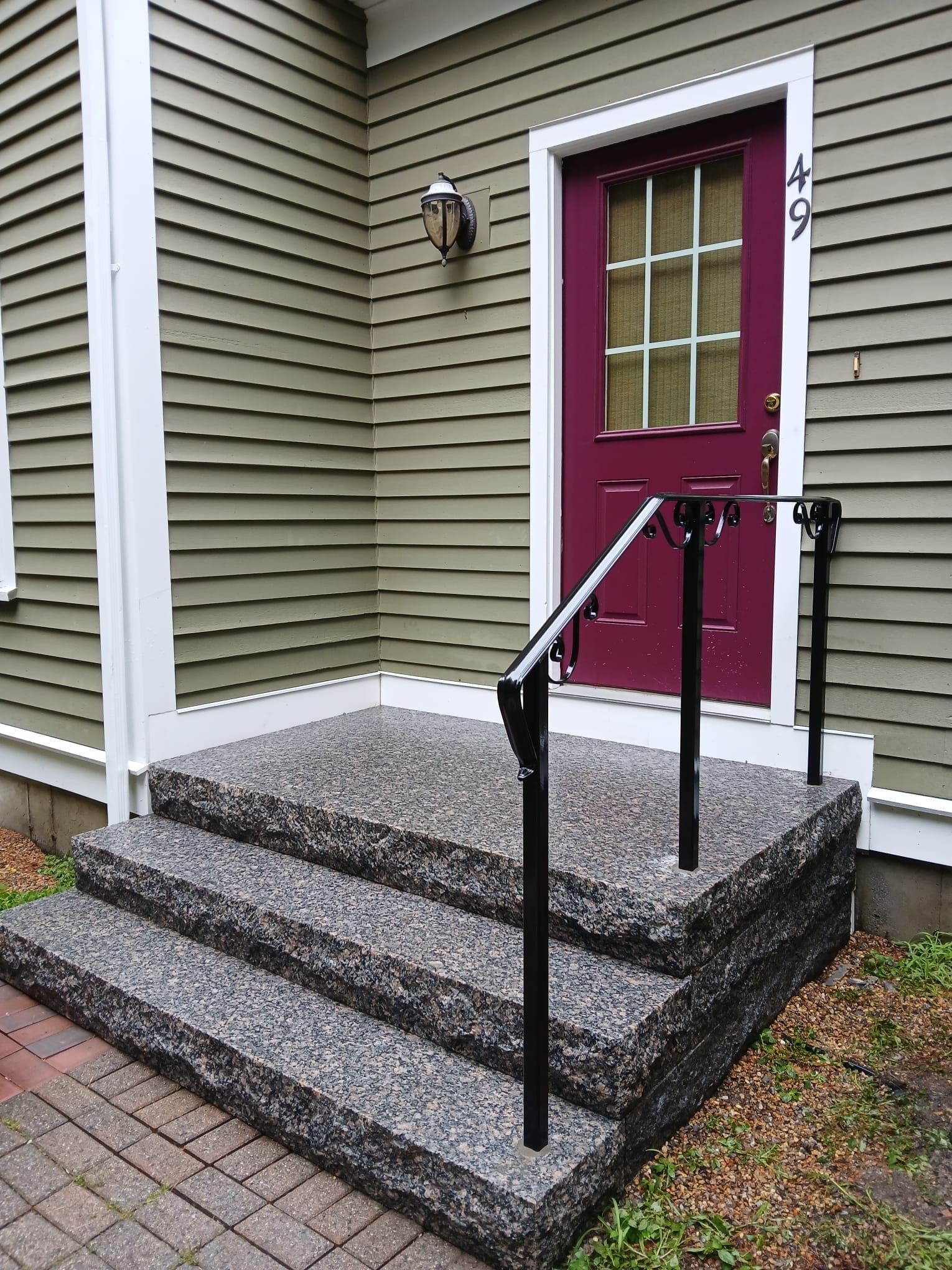 Front steps with black railings leading to a maroon front door on a beige house