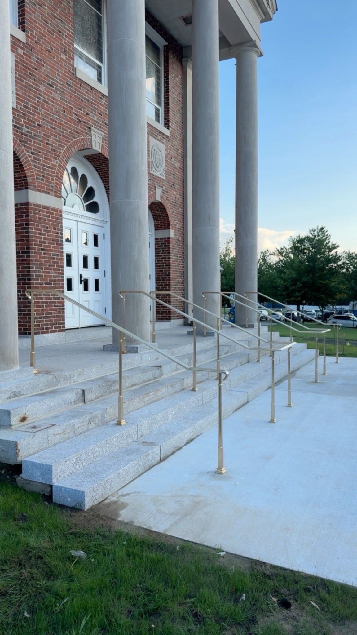 Brick building entrance with white arched doors, concrete steps, and metal handrails under tall columns