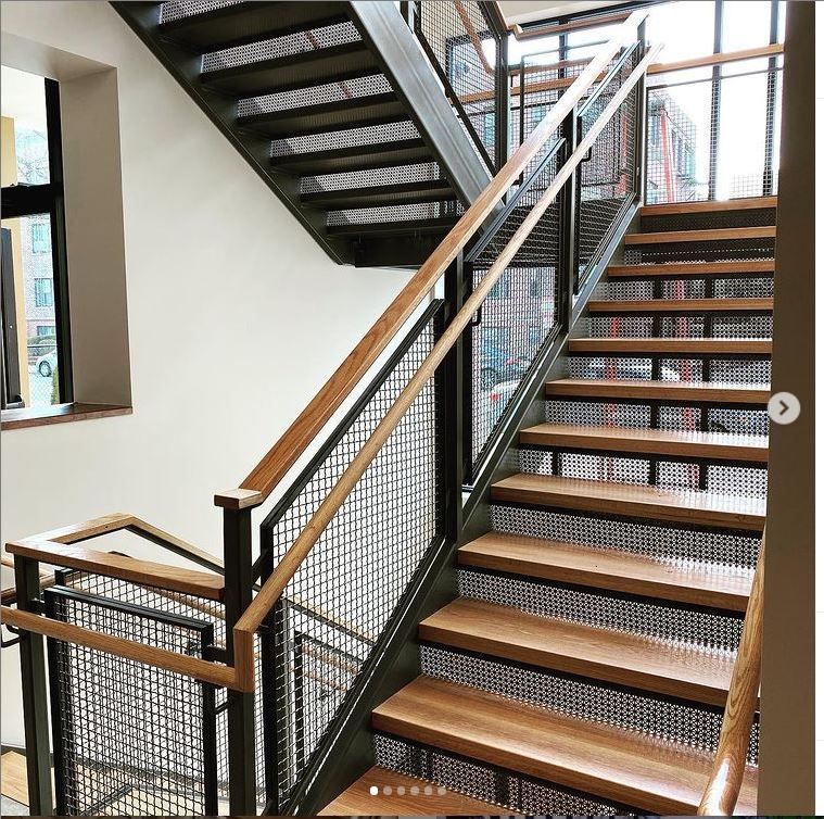 A modern interior staircase with wooden treads, black metal mesh railings, and a wooden handrail.