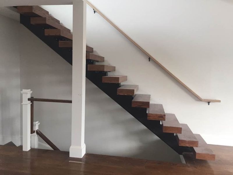 Modern staircase with wooden treads on a black steel stringer, white walls, and a matching wooden handrail.