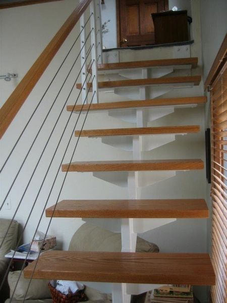 A staircase with wooden treads and a white central support, featuring a thin railing with horizontal metal cables.