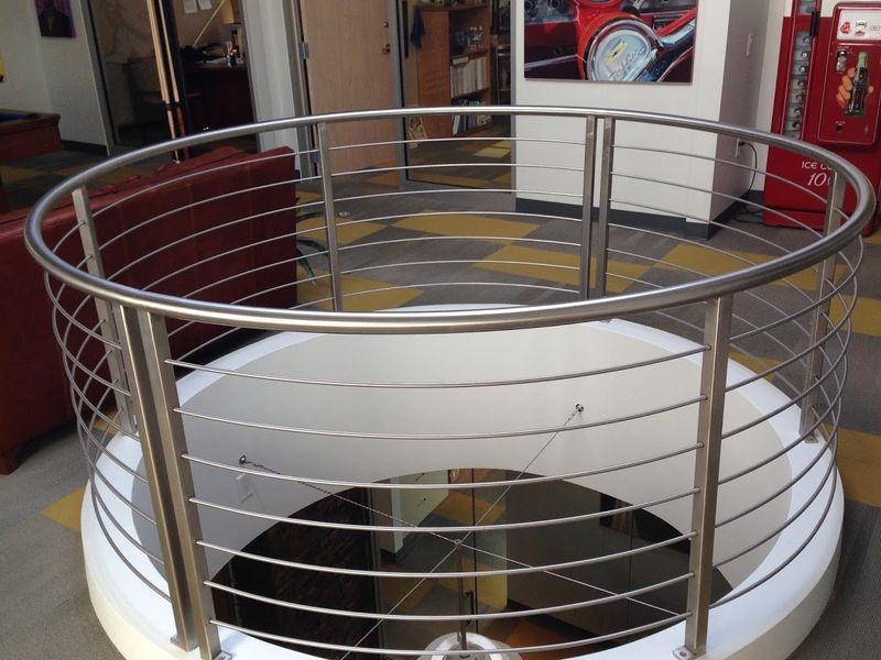 A curved, modern metal railing with horizontal cables surrounding an open circular floor cutout in an indoor space.