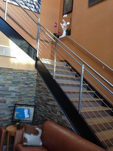 Modern staircase with wood steps, black metal stringers, and cable railings, set against a stone and orange wall.