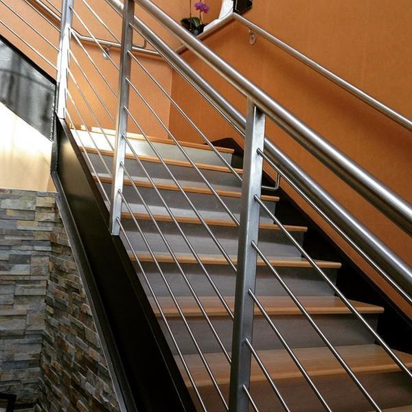 Staircase with light wood treads, metal railing with horizontal bars, and an orange wall alongside a stone-textured wall.