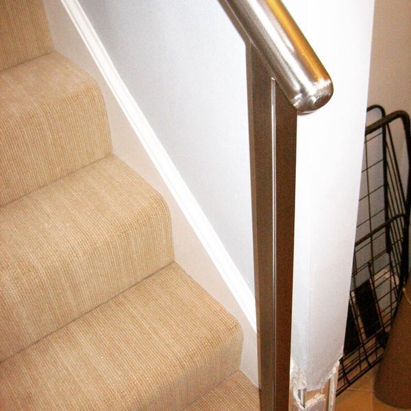 A beige carpeted staircase viewed from above, featuring a dark wooden newel post topped with a metallic handrail.
