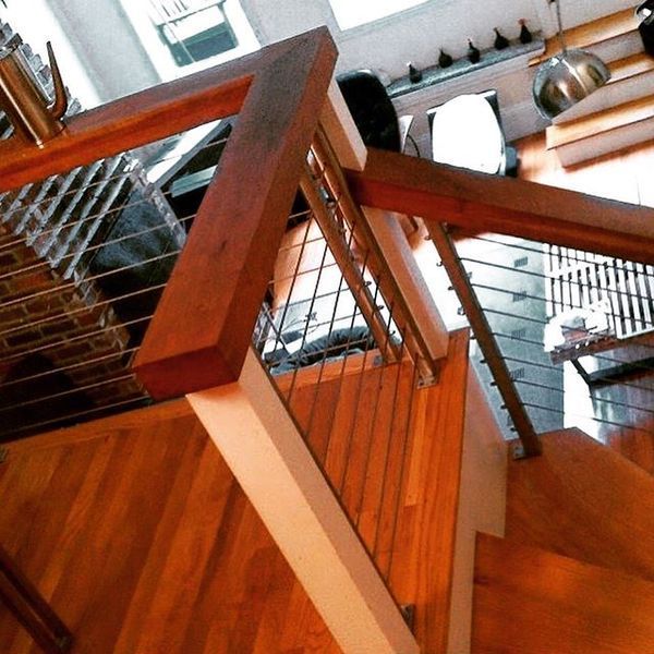 A wooden staircase with white posts and horizontal cable railings overlooking a room with hardwood floors.