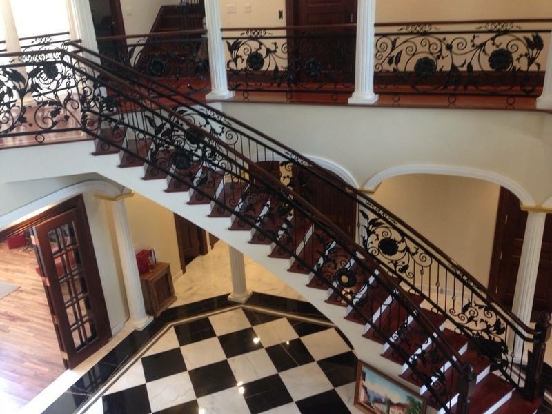 Grand indoor foyer with a curved wooden staircase featuring decorative black wrought iron railings over a checkered floor.