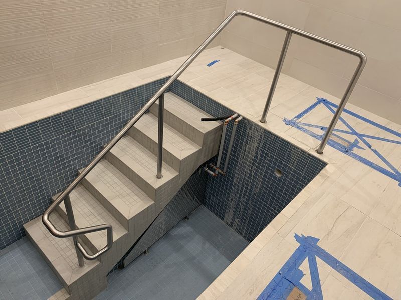 Concrete stairs leading down into a tiled pool area with a stainless steel handrail, during a construction phase.