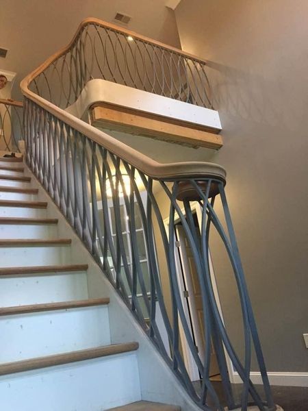 A staircase with a wooden handrail and curved, dark metal balusters leading up to a second-floor landing.