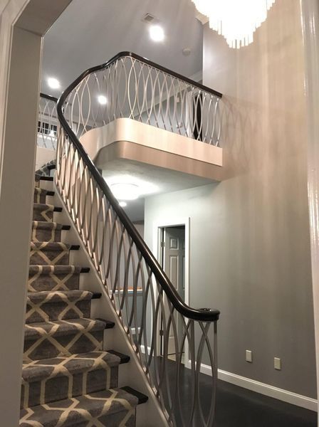 A curved staircase with a dark wooden handrail, patterned carpet, and decorative white metal railings in a foyer.