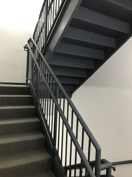 A view from the bottom of a stairwell featuring gray carpeted stairs and dark metal railings.