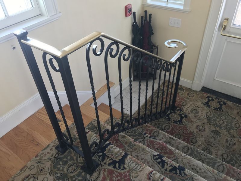 Black wrought iron staircase railing with a light wood handrail, situated on carpeted stairs next to an entryway.