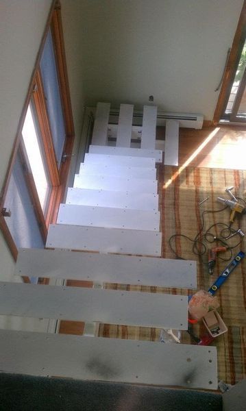 Top-down view of unfinished wooden stairs with white treads being installed in a room with a striped rug and tools.
