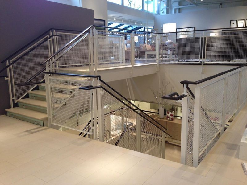 A two-story interior staircase with white metal mesh railings and dark handrails, leading down into a retail space.