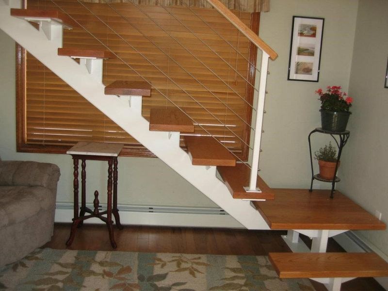 Open-tread staircase with white stringers, wooden steps, and wire railing beside a window and a small potted plant stand.