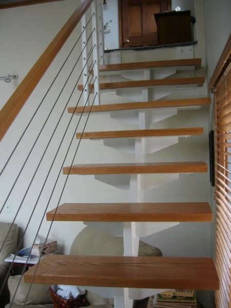 Modern floating staircase with light wood treads, a white central support spine, and a wire cable handrail.