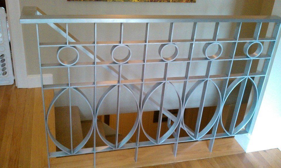 A silver, geometric metal stair railing featuring repeating circular and oval patterns on a wooden staircase.