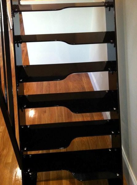Staircase with black, cut-out style steps between two dark railings, viewed from above looking down onto a wood floor.