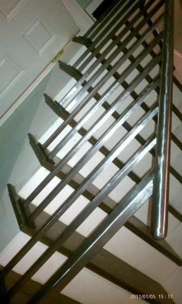 A view looking down a carpeted staircase with a metal handrail and decorative metal balusters.