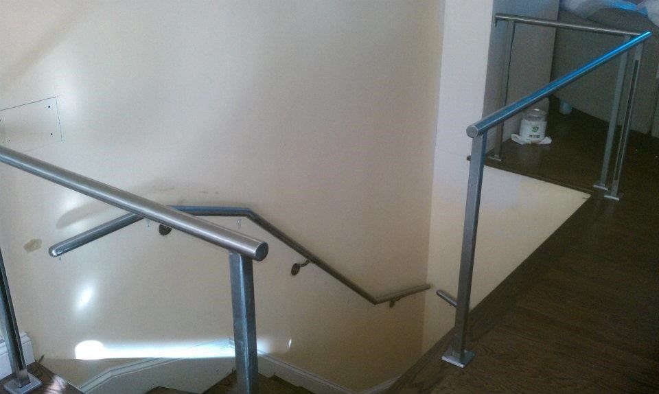 Stainless steel handrails mounted along a staircase against a plain wall, viewed from the top landing.