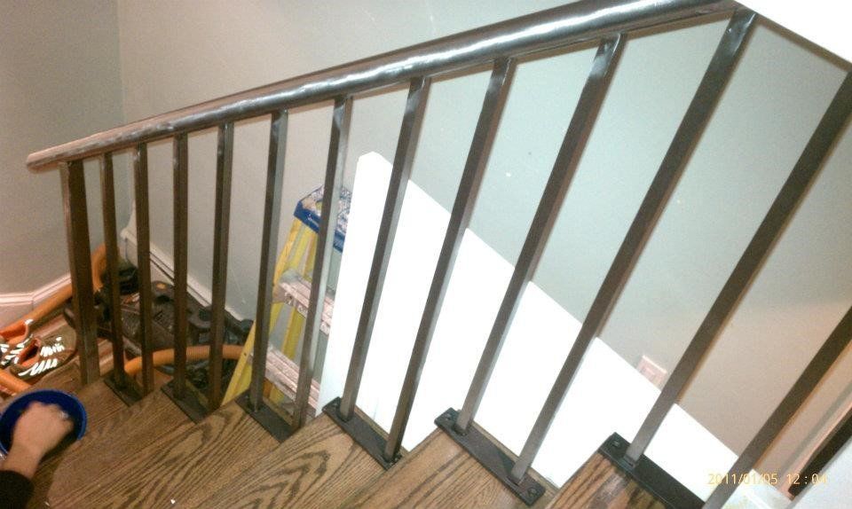 A metal staircase railing attached to wooden steps, with a hand holding a blue cleaning cloth in the lower corner.