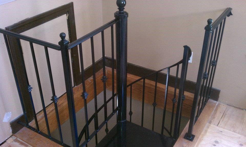 Black metal railing surrounding a wooden staircase opening in a home interior.