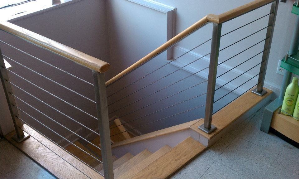 A staircase with wooden treads and a metal railing system featuring horizontal cables and a wooden handrail.