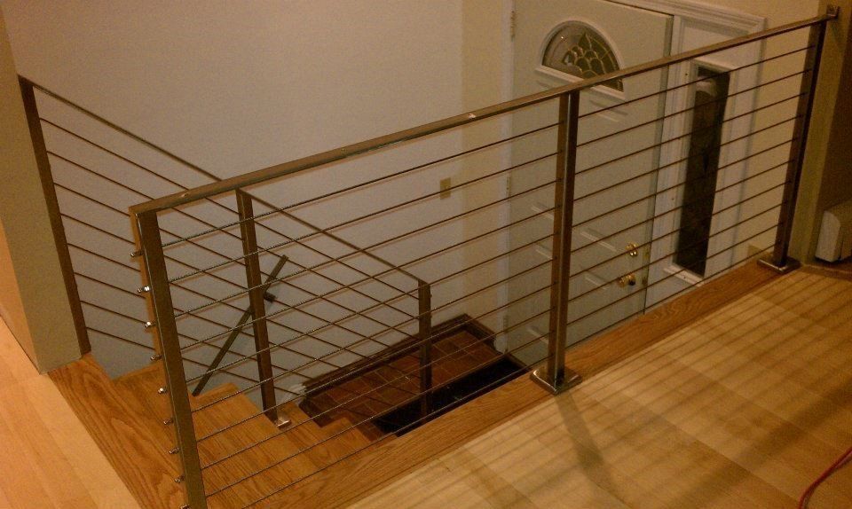 Modern staircase with wooden steps and a stainless steel cable railing system overlooking an entryway.