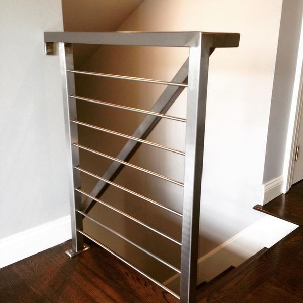 Modern stainless steel stair railing with horizontal cables, set against a white wall and dark wood flooring.