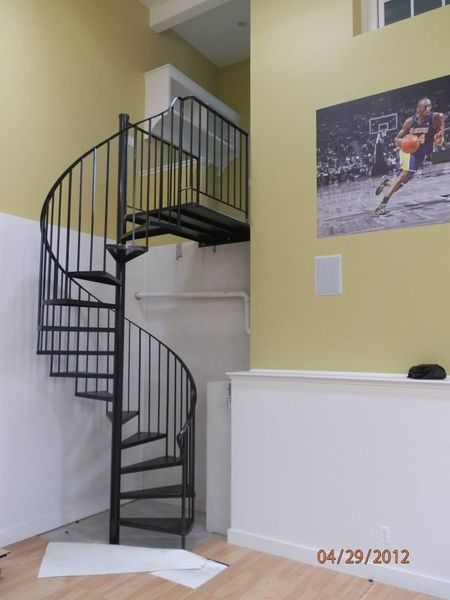 Black metal spiral staircase in a room with yellow walls, a basketball poster, and wood floors.