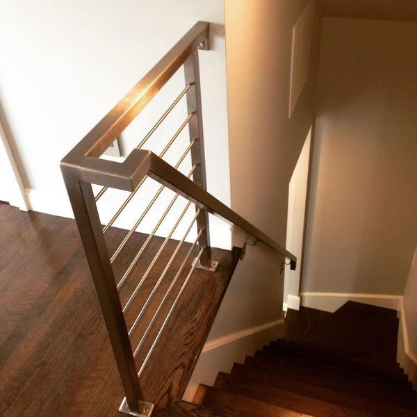 A modern staircase railing with horizontal metal cables and a square-profile frame, set above a dark wooden floor.