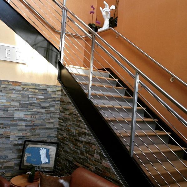 Modern staircase with wooden steps, metal railings, a stone accent wall, and orange decor in an interior space.