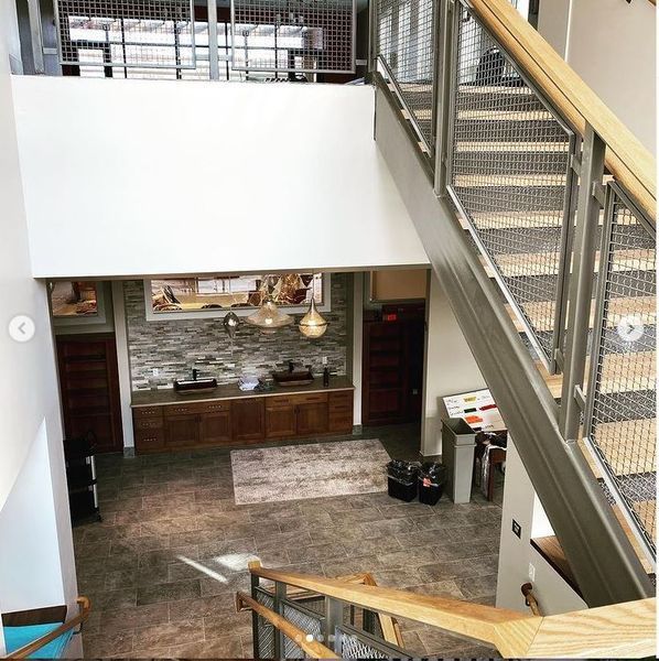 Staircase with metal railings and wooden handrails overlooks a lobby area featuring a stone backsplash and wooden cabinets.