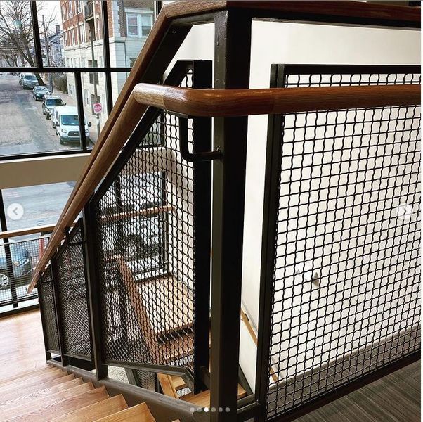 A staircase with wooden treads, a metal grid railing, and a warm-toned wooden handrail next to a window overlooking a street.