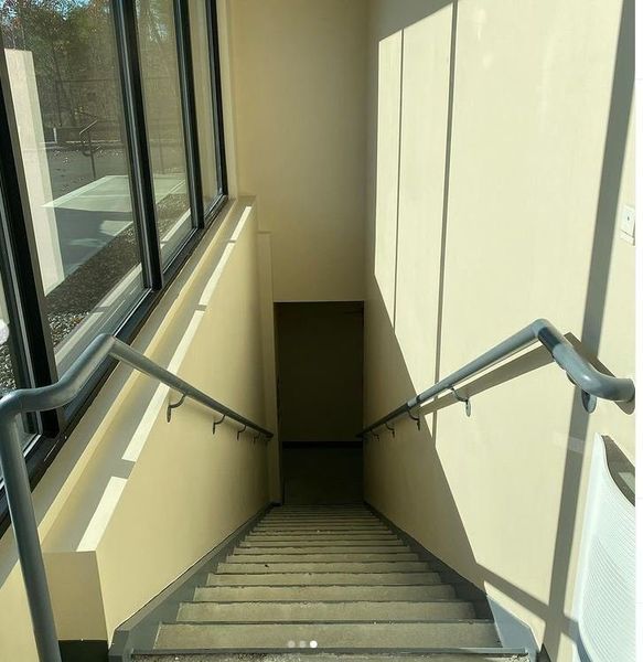 A staircase looking down, with a gray metal handrail on each side and light reflecting on the pale yellow walls.