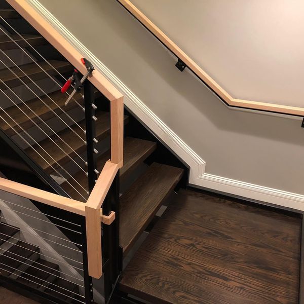 A staircase with dark wood steps, black metal posts, cable railings, and light wood handrails, including a wall-mounted rail.