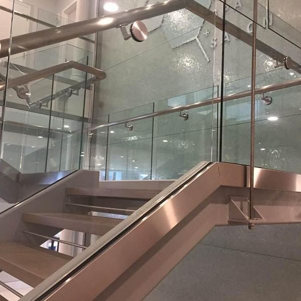 Modern staircase with wooden steps, metallic railings, and glass panels in a brightly lit indoor space.